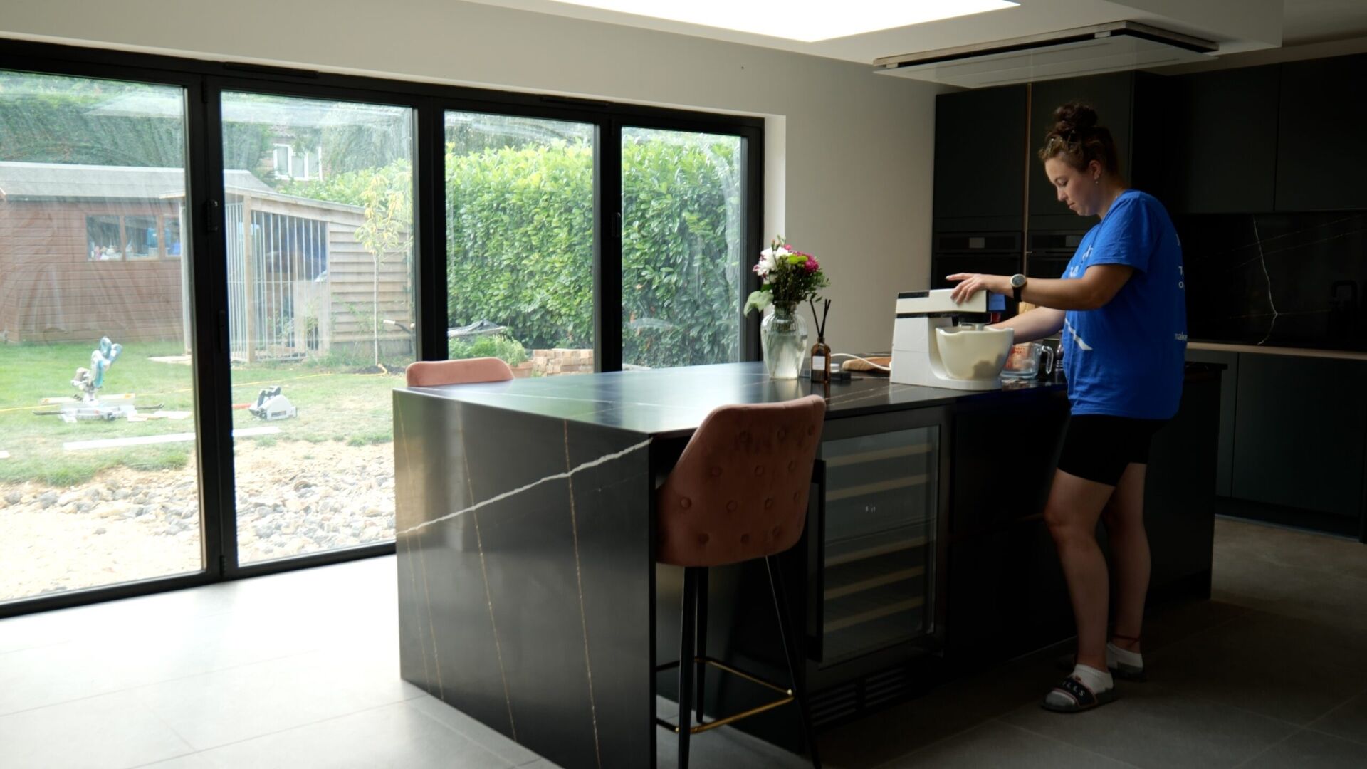 Testimonial kitchen with Sahara Noir Quartz waterfall island showing black surface with gold-toned veining, with Jessica standing beside the island