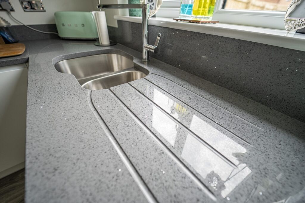 Grey speckled Quartz worktop with integrated drainer grooves leading into a stainless steel sink