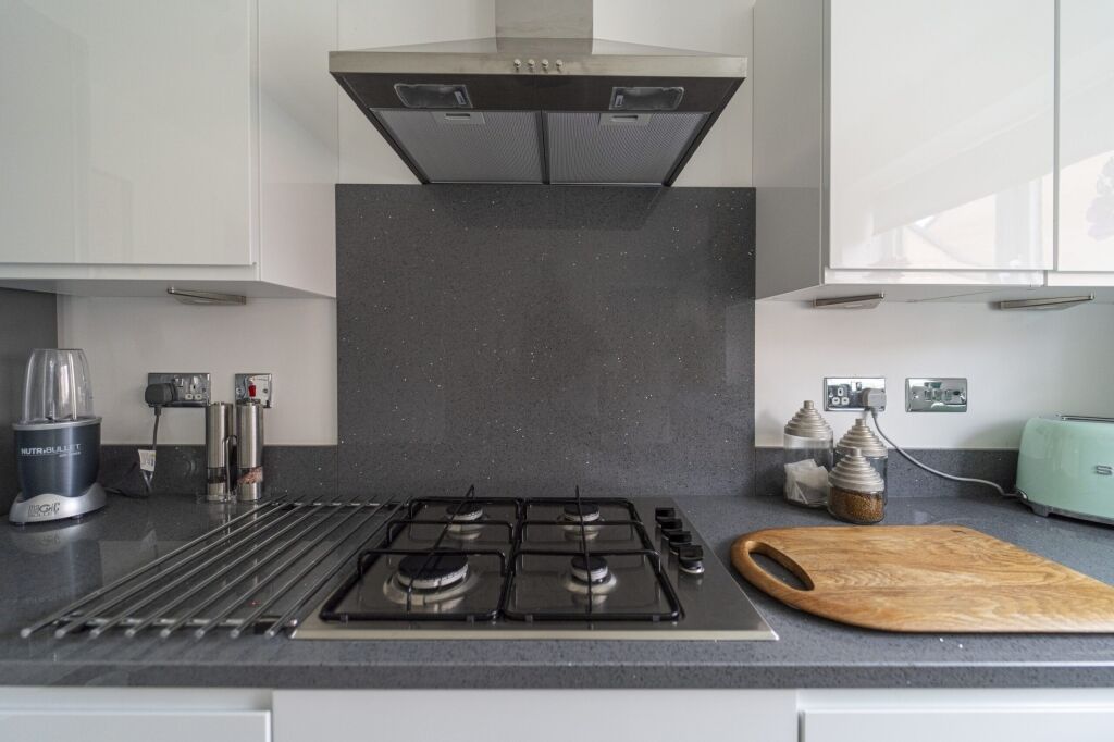 Grey speckled Quartz worktop with matching splashback behind a gas hob and cooker hood