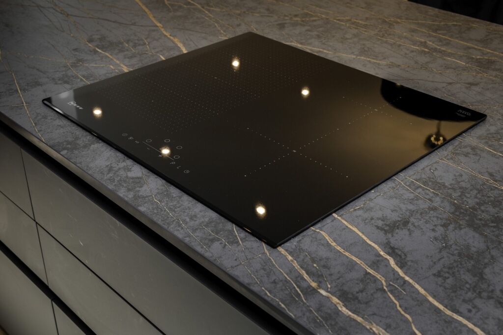 Close-up of a flush black induction hob set into a Laurent Porcelain worktop with gold veining.