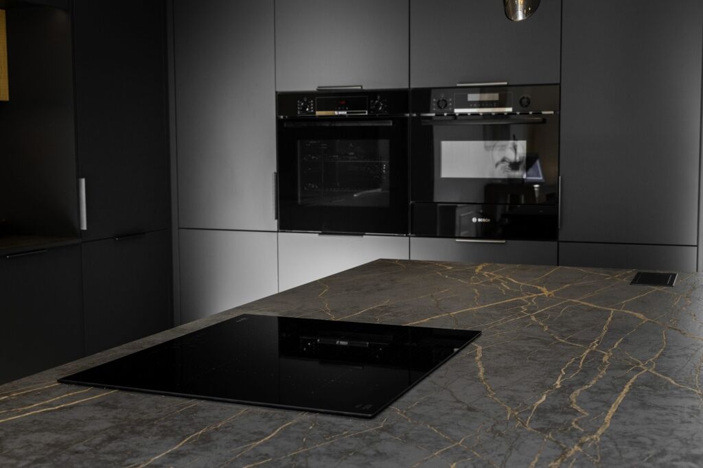 Laurent Porcelain worktop with gold veining fitted in a modern kitchen, featuring a flush black hob beside built-in ovens.
