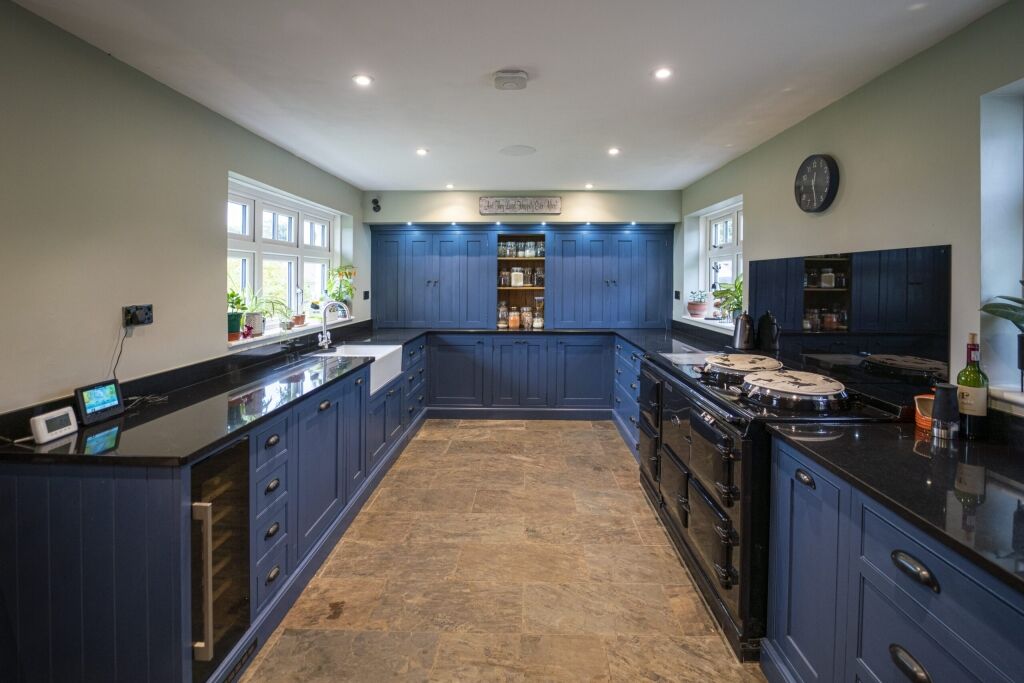 Wide perspective down a blue kitchen with Absolute Black Granite worktops on both sides, showing the sink run and cooking area at the far end.