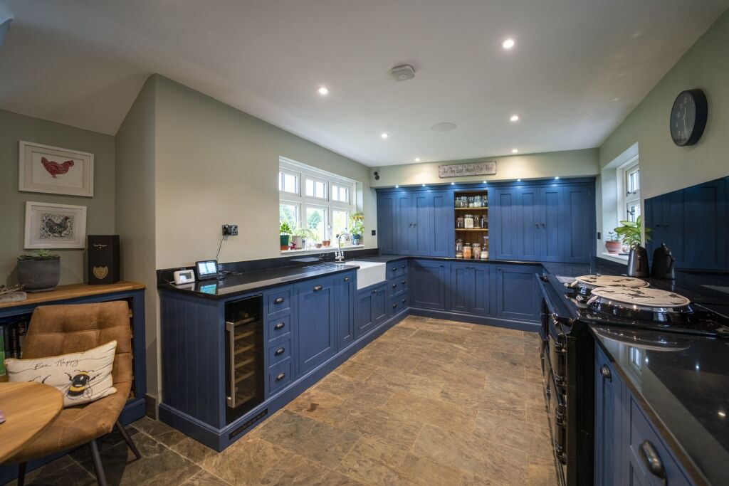 Full kitchen view with blue cabinetry and Absolute Black Granite worktops along the perimeter run, showing the sink area and a drinks fridge under the worktop.