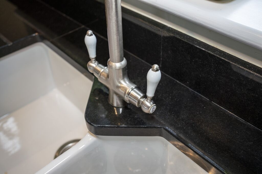 Close up of a kitchen tap over a sink with Absolute Black Granite worktop and matching Granite upstand, showing the polished finish around the corner.