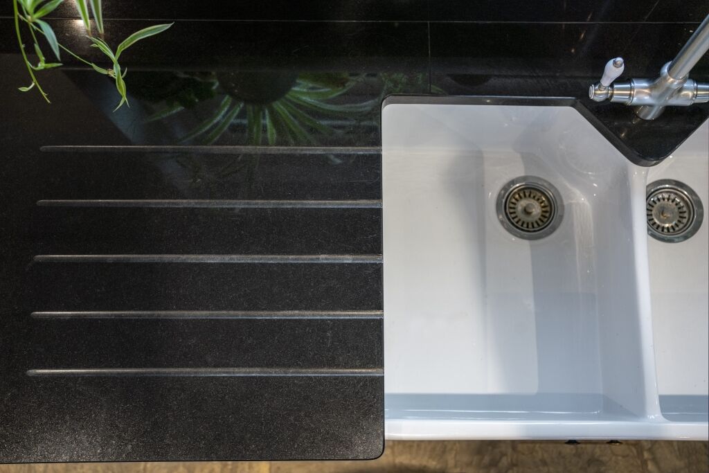 Close up of Absolute Black Granite worktop with precision cut drainer grooves next to a white sink, showing the polished finish and clean lines.