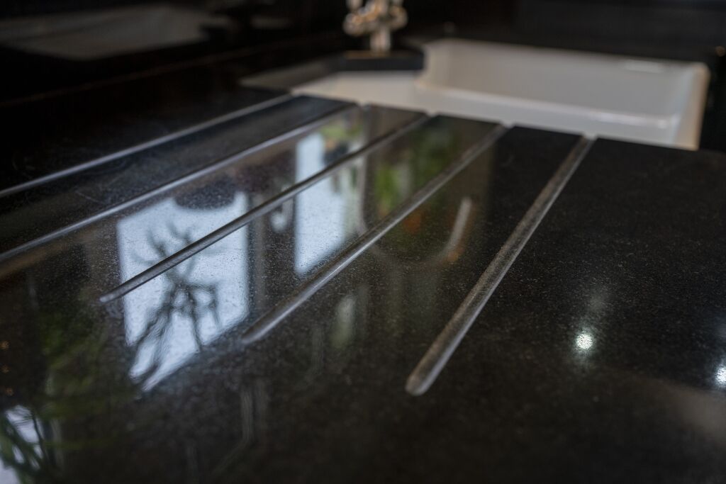 Close up of Absolute Black Granite worktop showing precision cut drainer grooves with reflections on the polished surface near the sink.