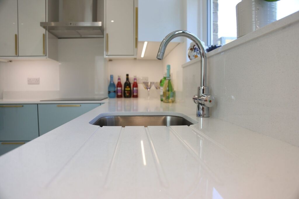 Close-up of Dover White Quartz drainer grooves beside a stainless steel sink and chrome tap