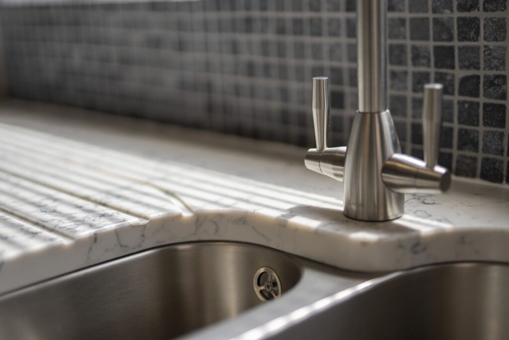 Close-up of Arabescato Quartz drainer grooves beside a stainless steel sink and tap showing grey veining
