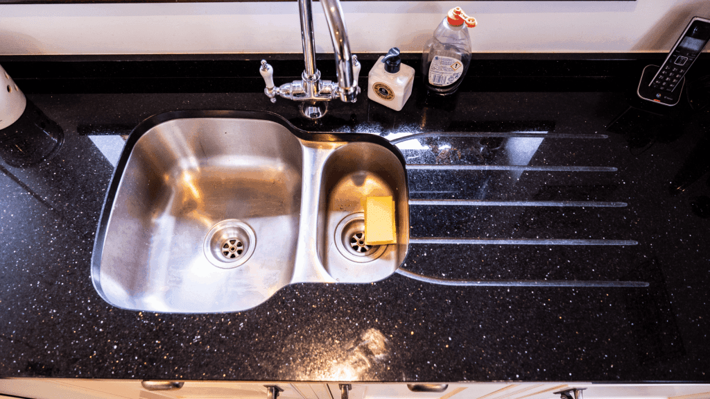 Sink area in Star Galaxy Granite with drainer grooves and a polished finish, showing the sparkling fleck pattern beside a stainless steel sink.