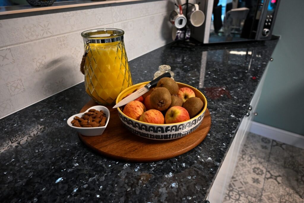 Styled close up of Blue Pearl Granite worktop with a breakfast tray, fruit bowl and orange juice, showing the dark speckled Granite pattern.