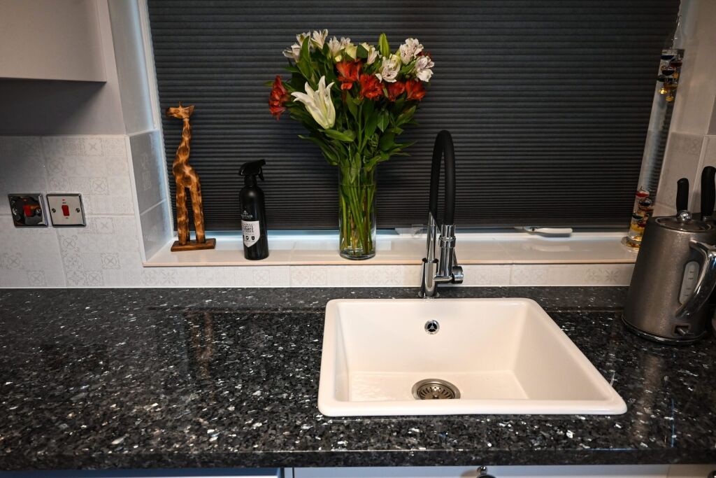 Sink area in Blue Pearl Granite with a white inset sink and black tap, showing the speckled Granite surface and a vase of flowers by the splashback.