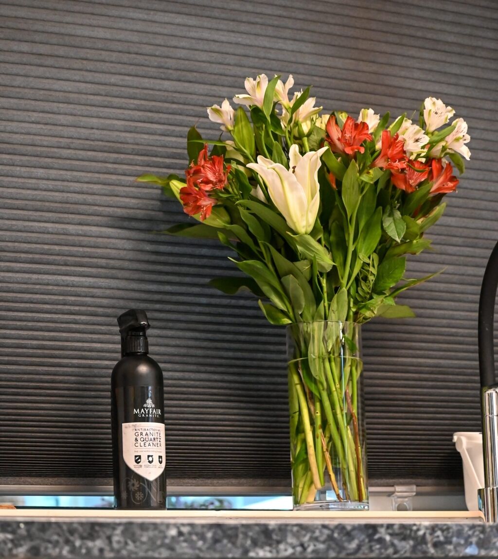 Blue Pearl Granite worktop detail with a vase of flowers and a wine bottle, showing the speckled Granite surface against a dark splashback.