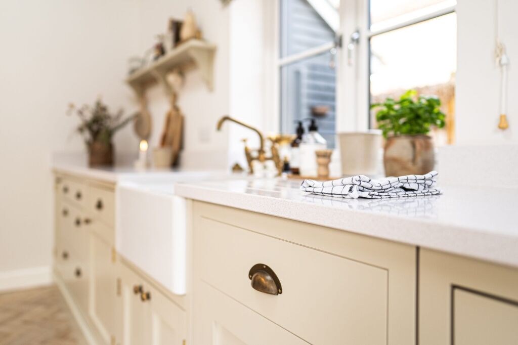 Ice White Quartz worktop on a sink run with a farmhouse sink and brass tap in a bright kitchen
