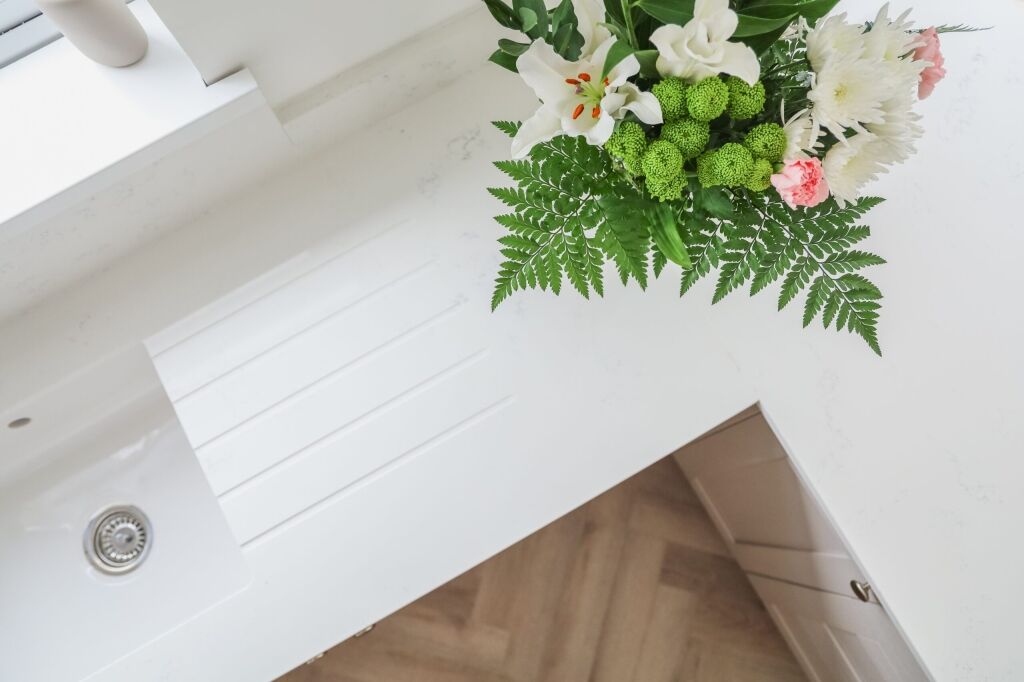 Bluetta Carrara Quartz worktop corner close-up showing a smooth edge and clean white finish near flowers