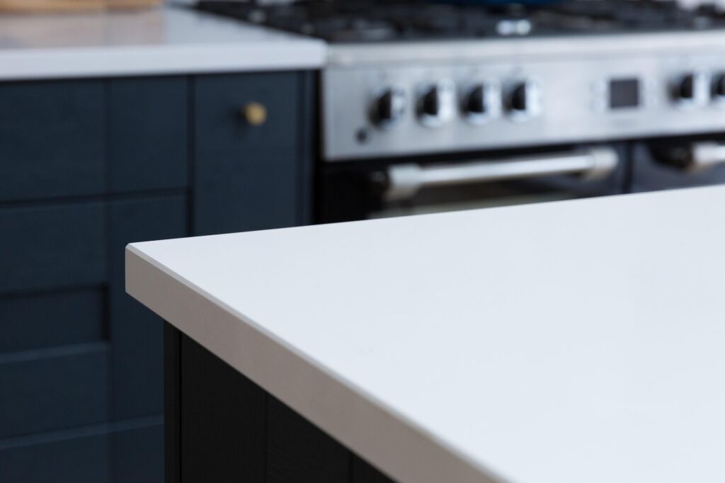 Blanco Zeus Quartz worktop edge close-up showing a crisp white surface above dark blue cabinetry