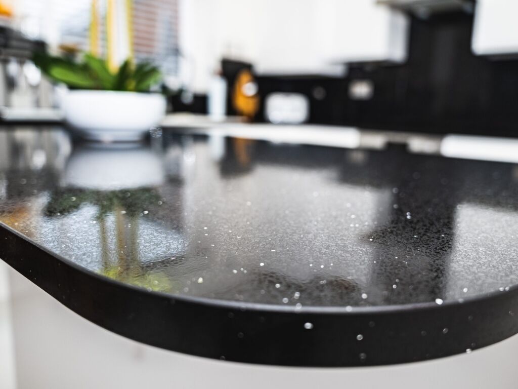 Black Starlight Quartz island edge close-up showing a curved front profile and sparkle flecks in the polished black surface