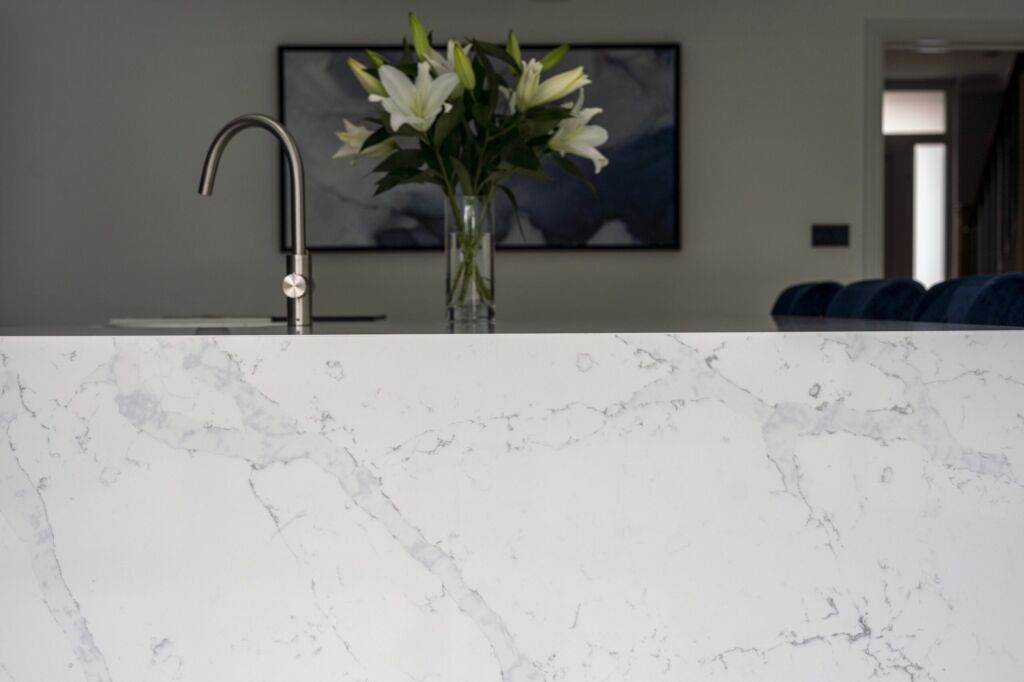 White Calacatta Quartz waterfall island showing grey veining with chrome tap and flowers in the background