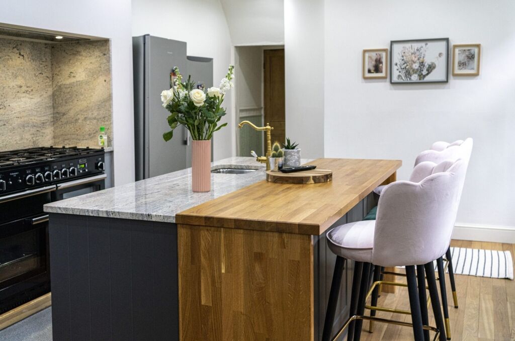 Angled view of an Ivory Fantasy Granite island worktop with sink, showing the Granite surface, timber waterfall end and seating area in a modern kitchen.
