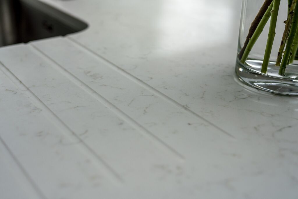 Drainer grooves cut into Carrara Quartz worktop beside stainless steel sink