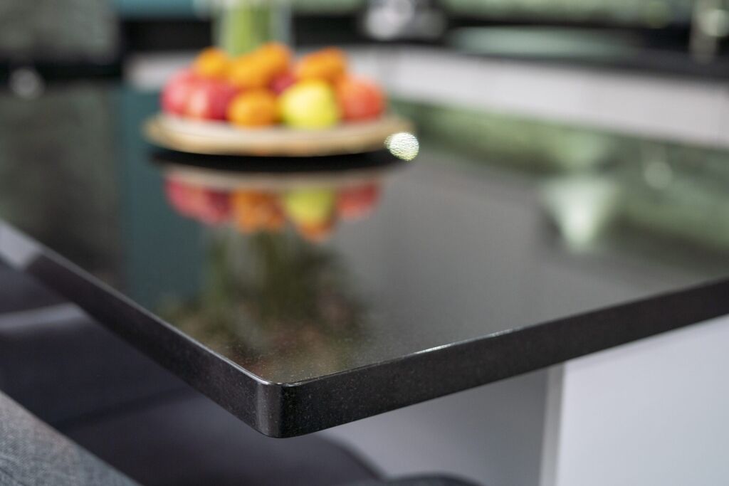 Close up of the polished edge of an Absolute Black Granite island worktop with a fruit bowl in the background, showing the deep black tone and glossy finish.