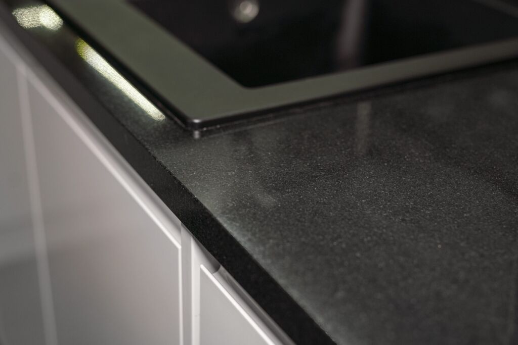 Close up of an Absolute Black Granite worktop corner with a polished finish, showing the edge detail beside an inset hob in a modern kitchen.