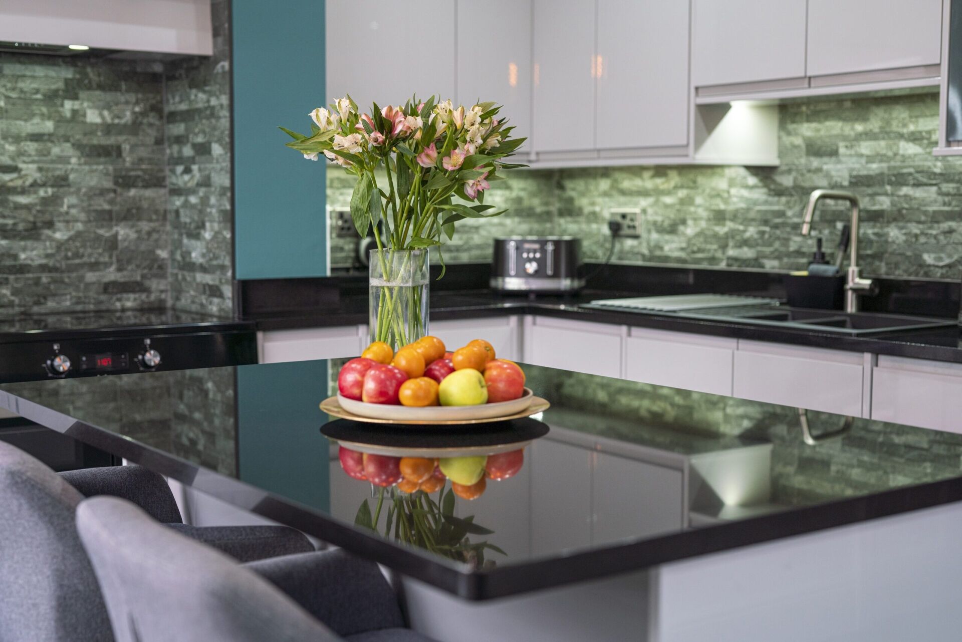 Modern kitchen scene with an Absolute Black Granite island worktop and curved corner, styled with fruit and flowers to show the polished surface.