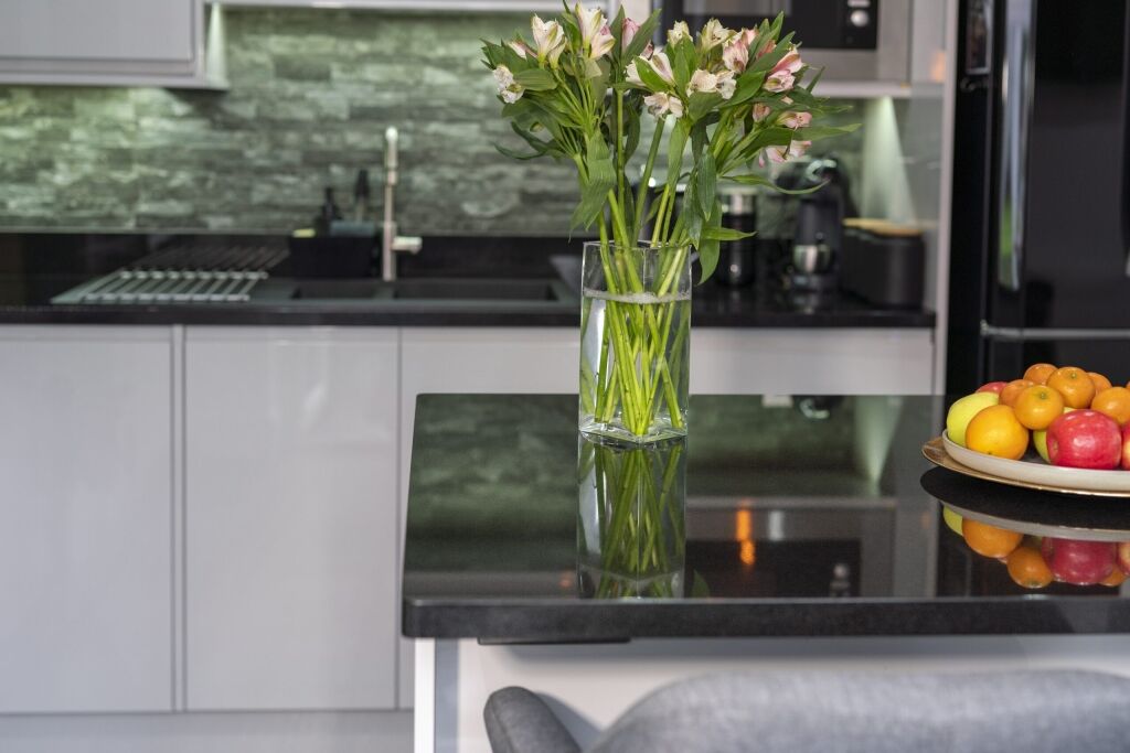 Close up of an Absolute Black Granite island worktop with a polished reflective finish, styled with a vase of flowers in a modern kitchen.