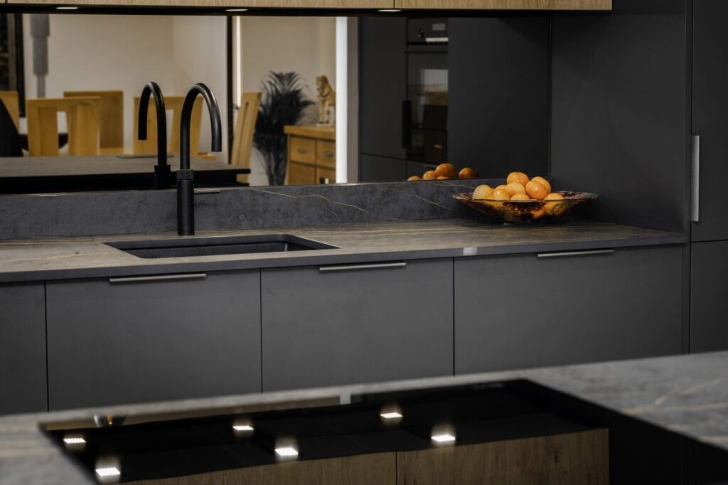 Laurent Porcelain worktop installed along the sink run with a black tap, sink and fruit bowl in a modern dark kitchen.