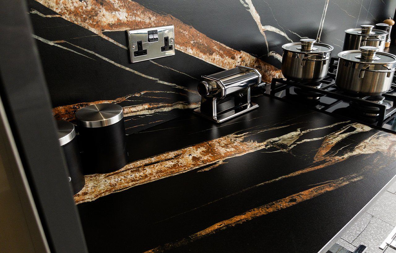 Noir St Laurent Porcelain worktop and splashback installed with strong amber veining, shown with small appliances on the counter.