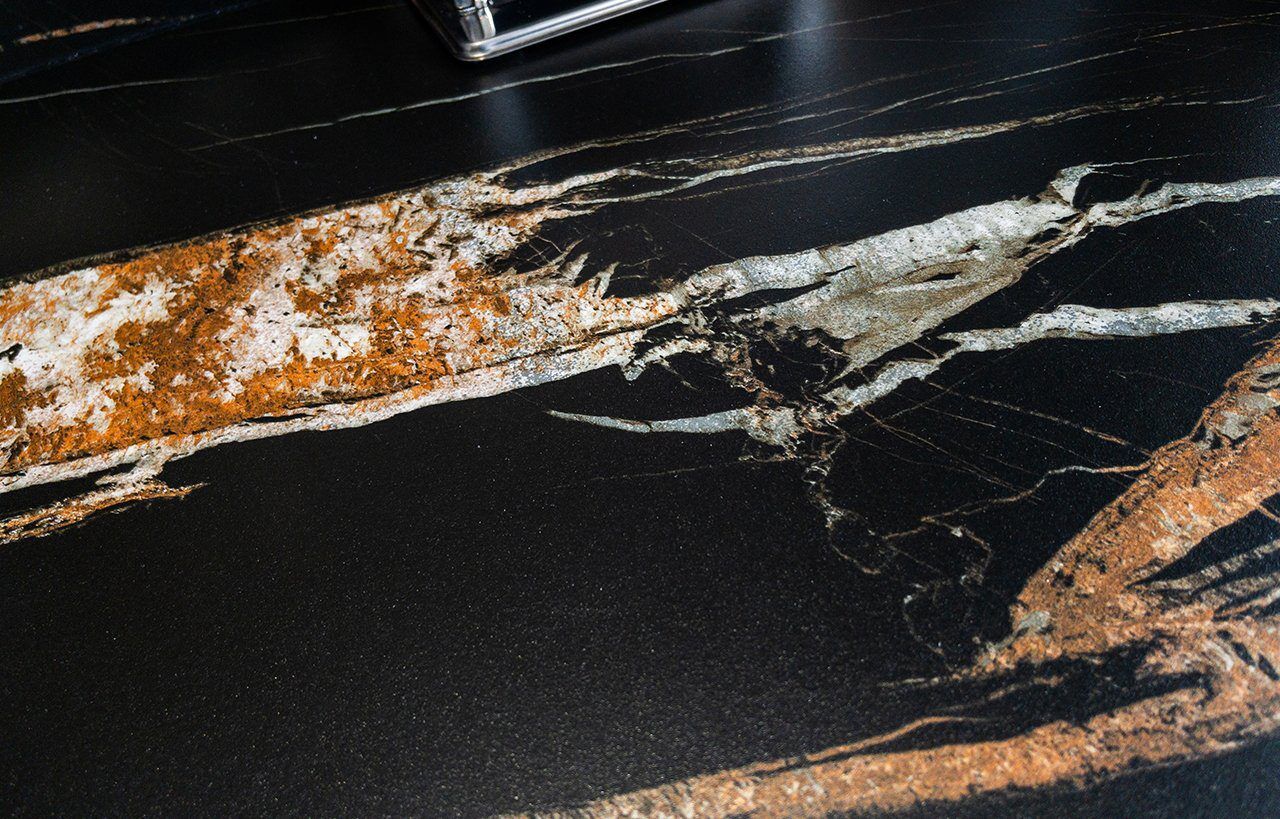 Noir St Laurent Porcelain close-up showing a dramatic amber vein running across a deep black surface near the hob area.