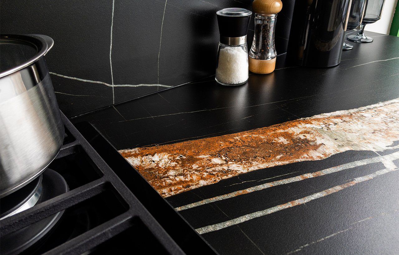 Noir St Laurent Porcelain worktop surface detail with black background and warm coppery veining beside countertop items.