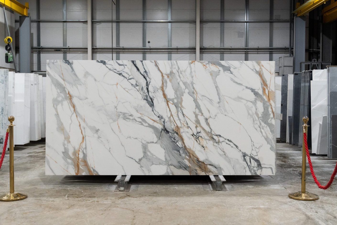 Calacatta Gold Borgnini Porcelain full slab on a display stand, showing a white marble effect background with grey veining and gold accents