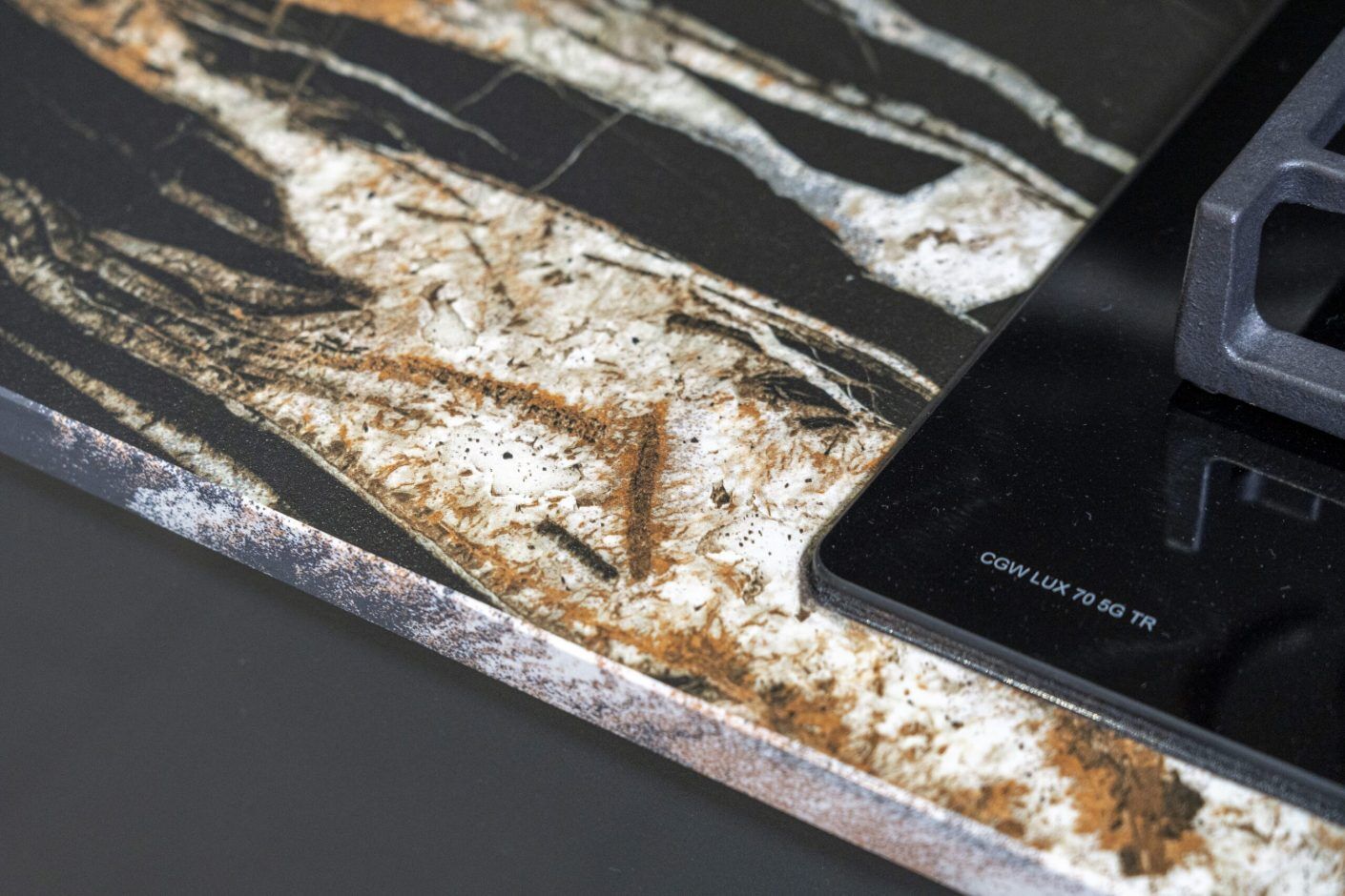 Noir St Laurent Porcelain worktop edge close-up with bold gold, copper and white veining on a deep black surface beside the hob.