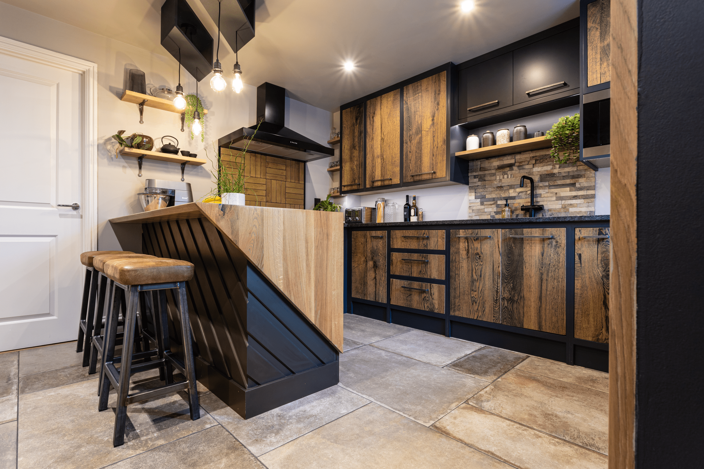Wide angle kitchen view with Steel Grey leather Granite worktops and an island breakfast bar, showing rustic wood cabinetry, bar stools and stone effect flooring.