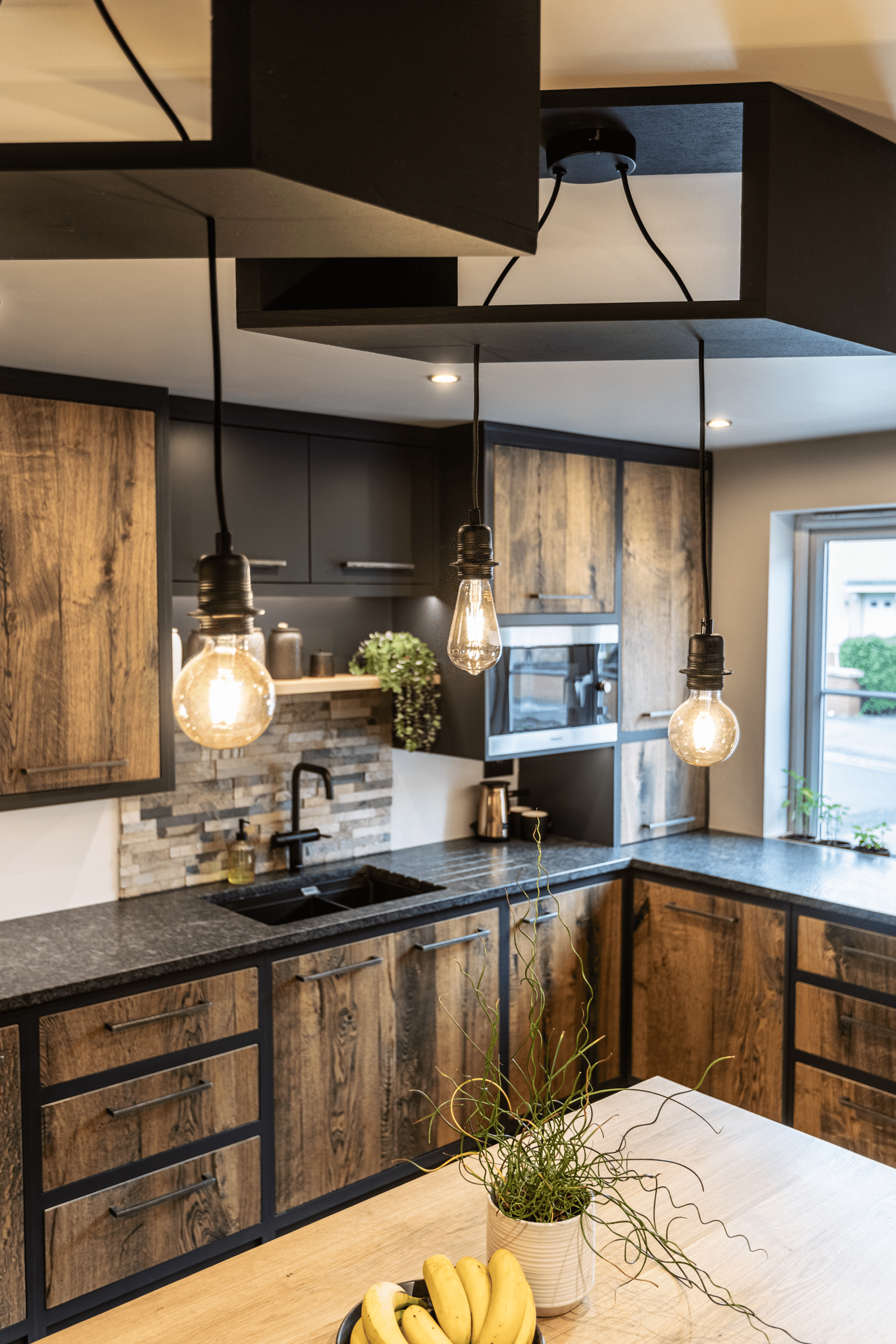 Corner kitchen view with Steel Grey leather Granite worktops and matching splashback detail, shown with rustic wood cabinetry and pendant lights above the worktop.