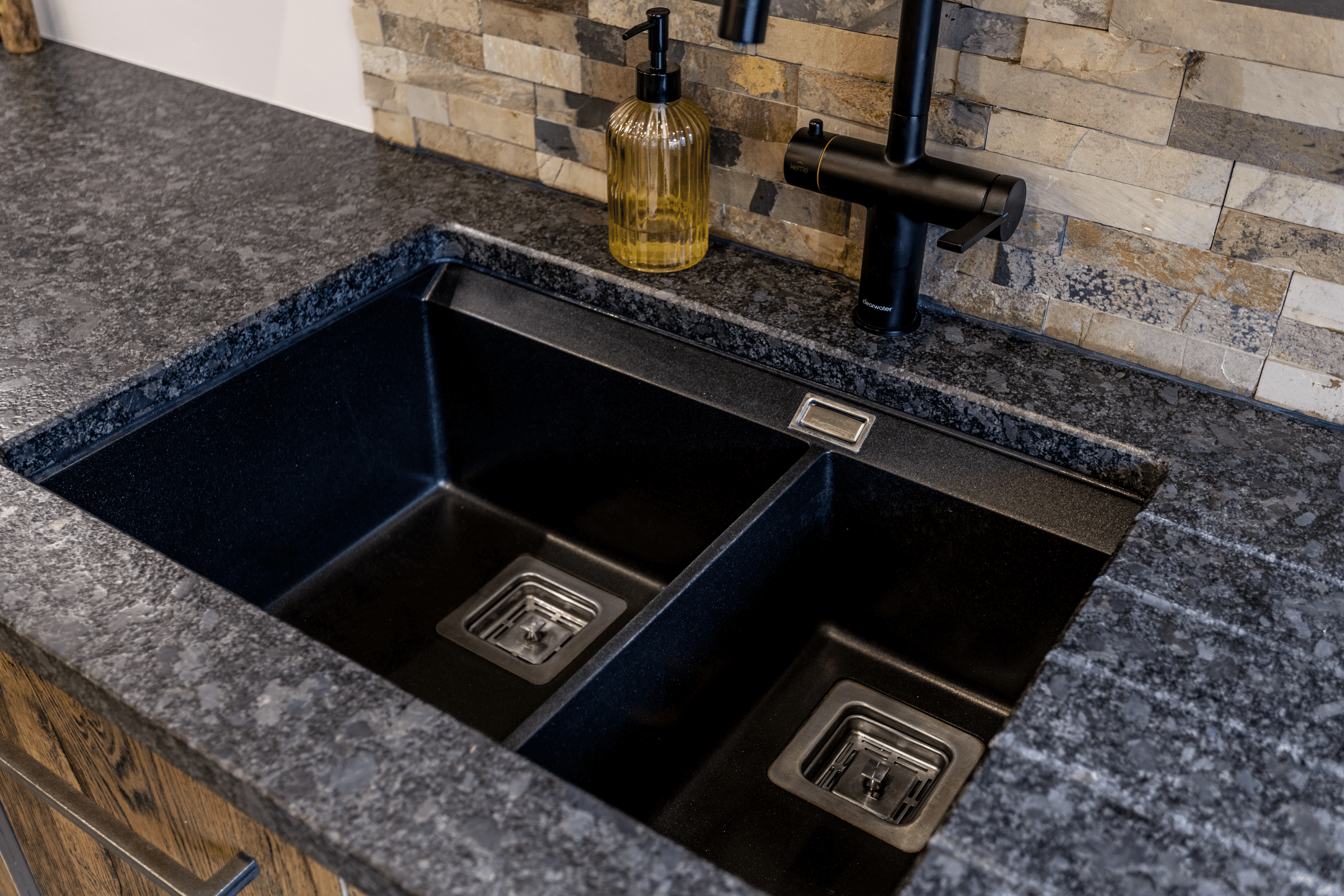 Close up of an undermount double bowl sink set into Steel Grey leather Granite worktop, showing the textured finish and clean cut-out lines.