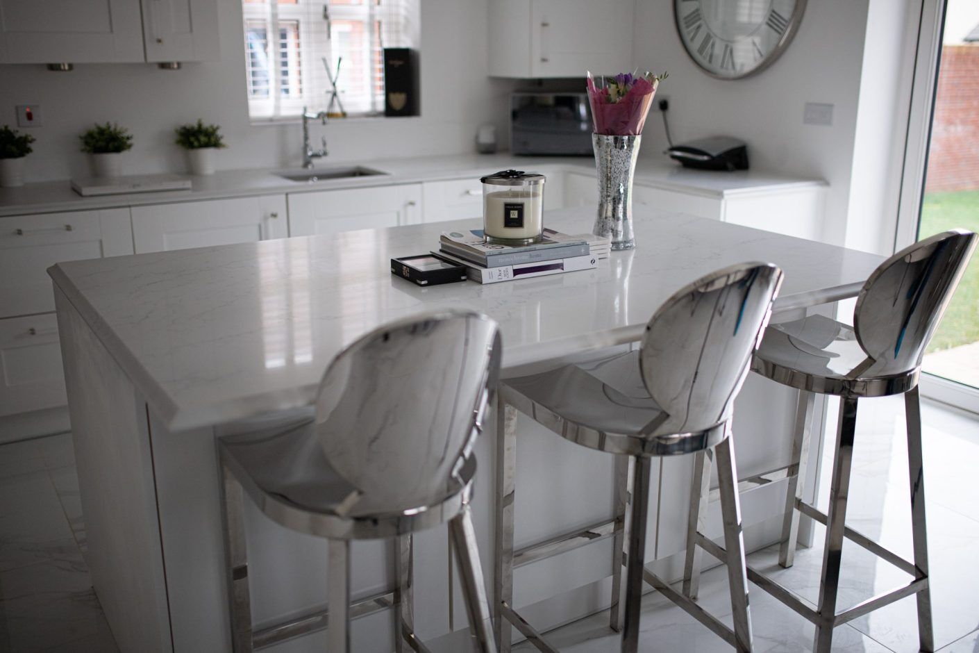 Modern kitchen featuring Statuario Bianco Porcelain island with bar stools and bright white cabinetry