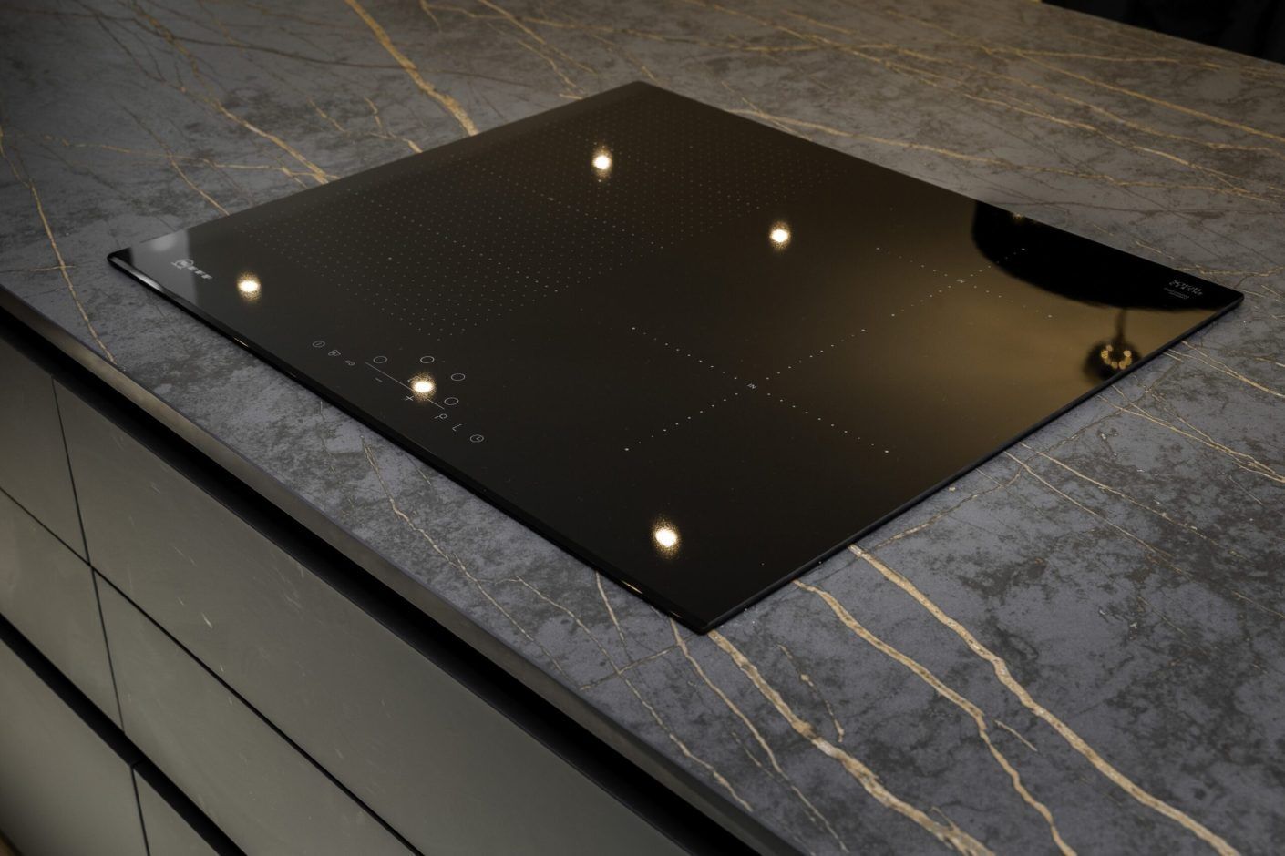 Laurent Porcelain worktop with gold veining and a flush black induction hob in a modern dark kitchen.