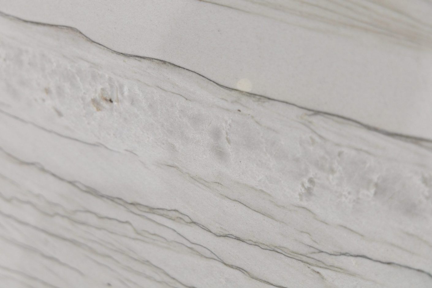 Close up slab photo of Bianco Macaubas Granite showing sweeping grey veining and a larger mineral feature across a pale stone background.