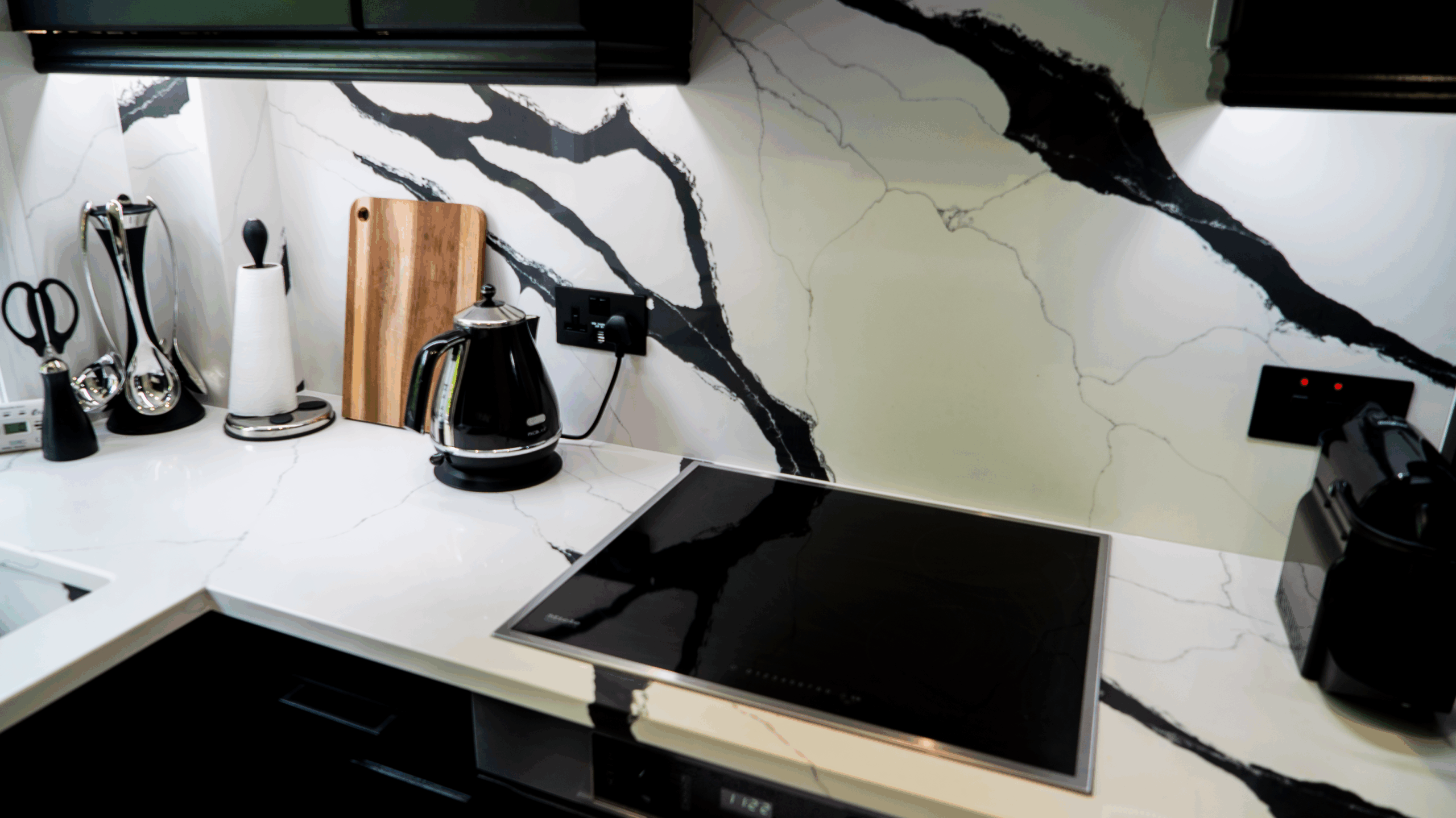 Black Calacatta Quartz worktop and splashback with bold black veining behind an induction hob in a modern kitchen