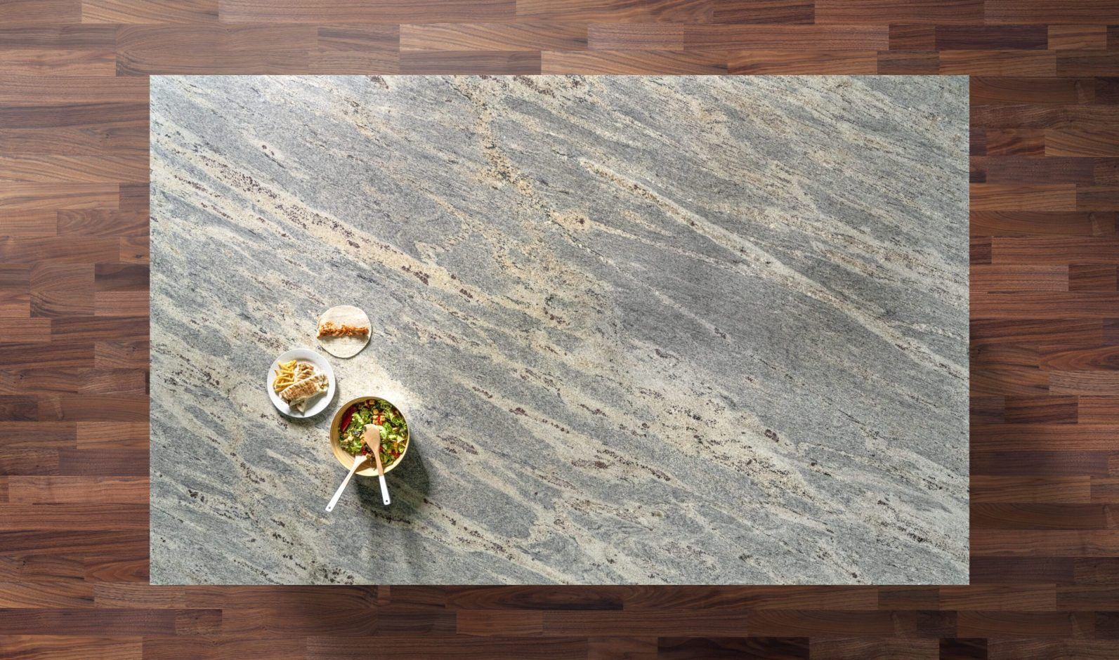Overhead view of a Kashmir White Granite worktop showing soft grey veining and warm mineral flecks, photographed from above with a small styled tray in the corner.