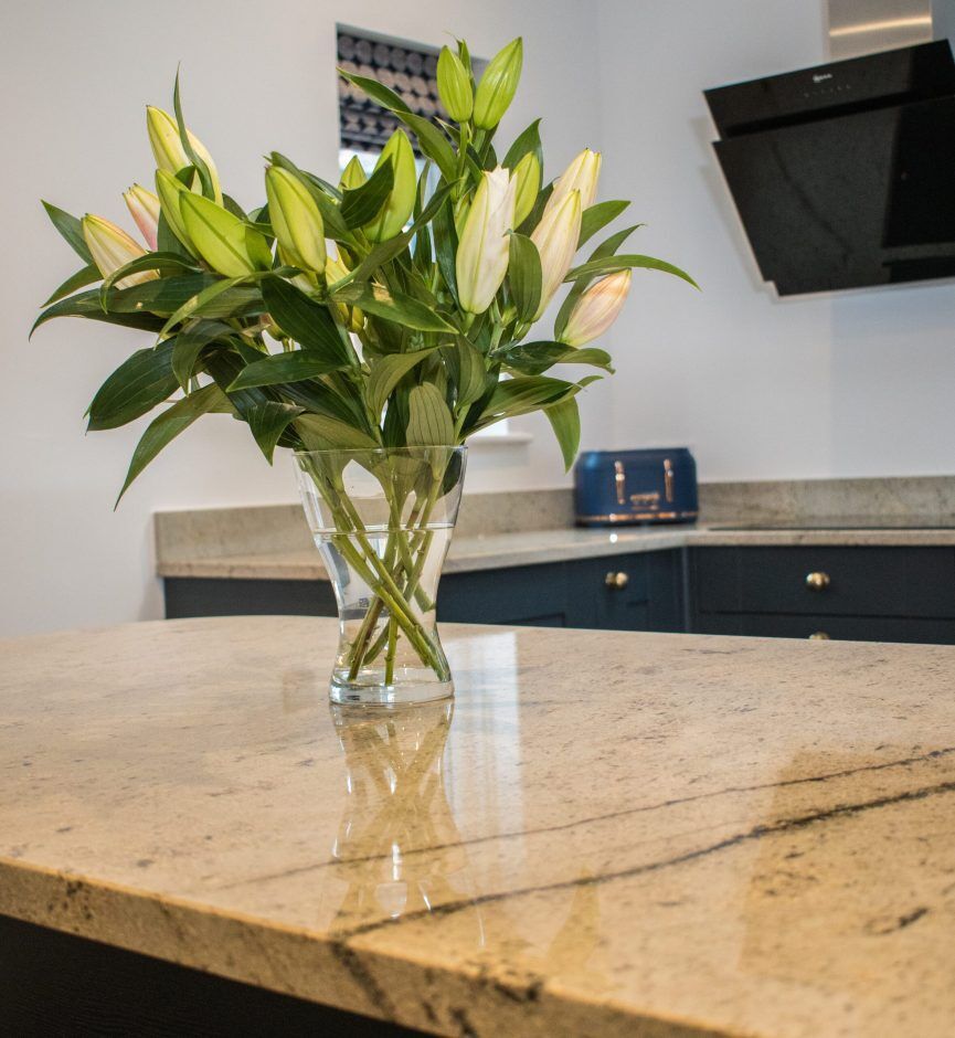 Close up of an Ivory Spice Granite island worktop with a vase of flowers, showing warm cream tones, soft veining and a polished reflective finish.