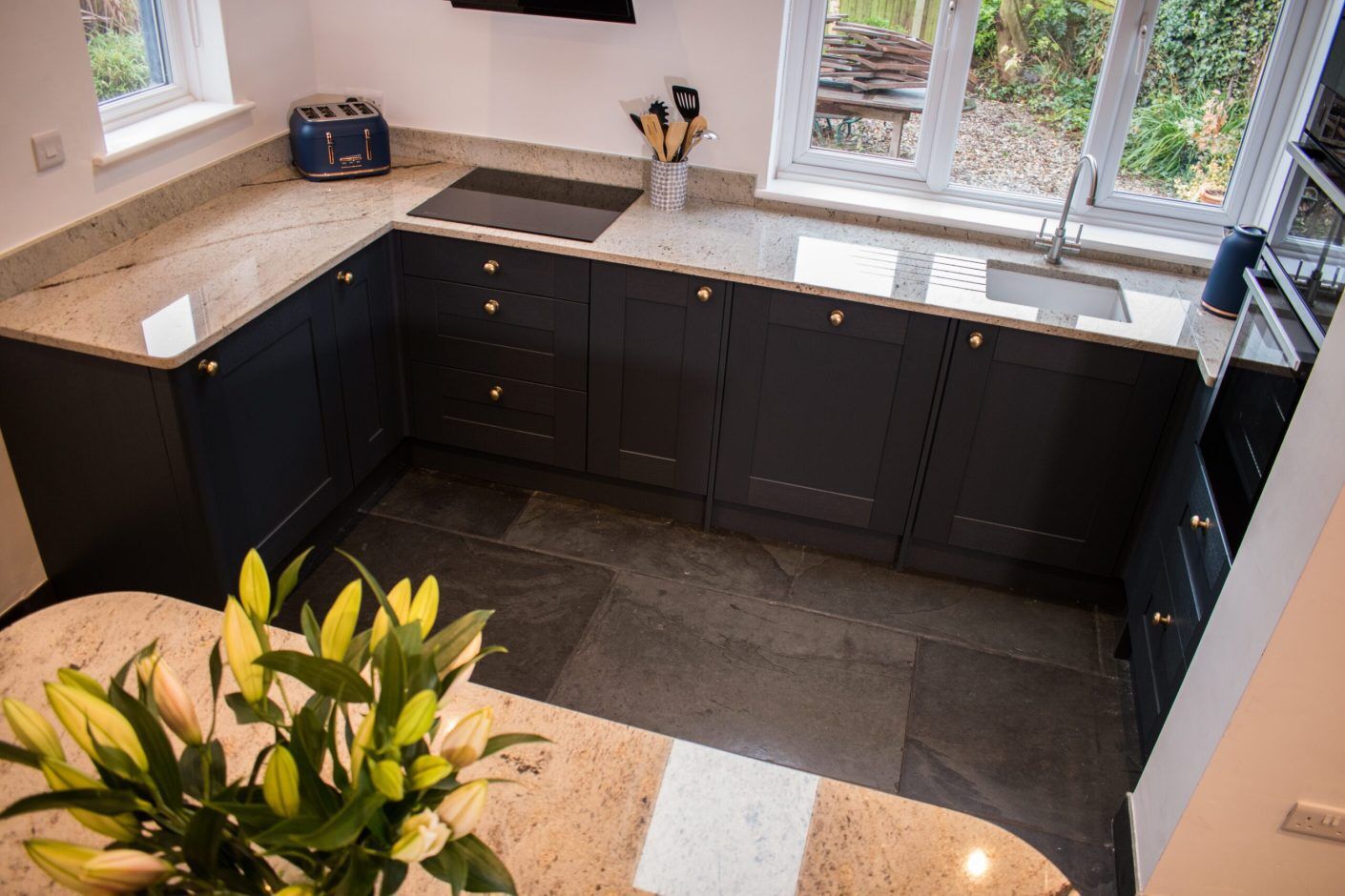 Sink run view with Ivory Spice Granite worktops on dark cabinetry, showing the polished Granite surface along the window wall and kitchen corner.