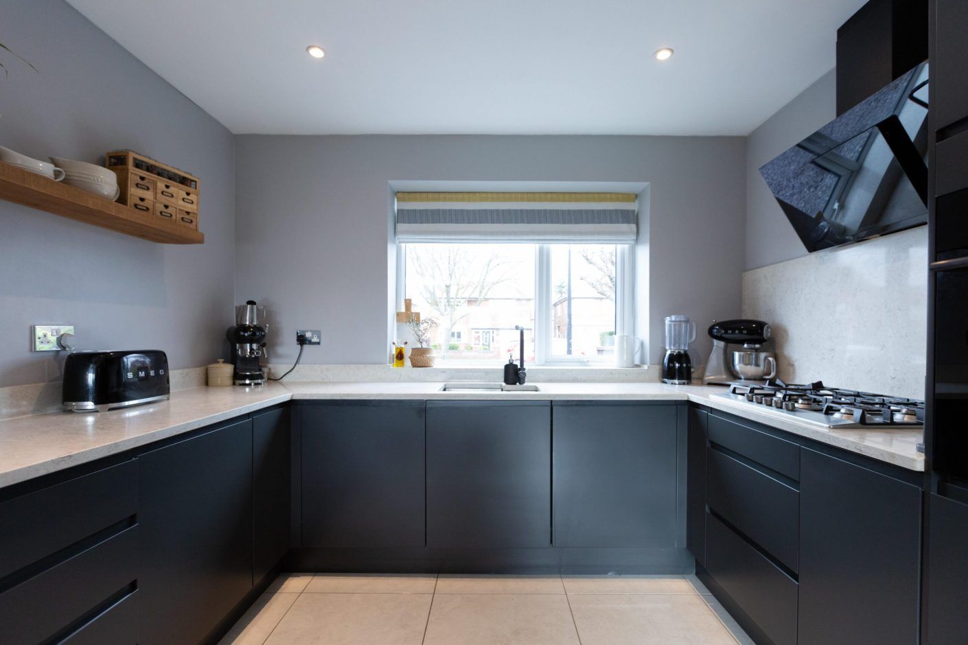 Grey Drift Quartz worktops fitted to a U-shaped kitchen with a window sink area and dark cabinetry