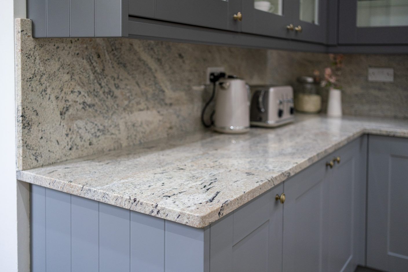 Corner view of Ivory Fantasy Granite worktop with matching Granite upstand, shown with kettle and toaster on a worktop run in a modern kitchen.
