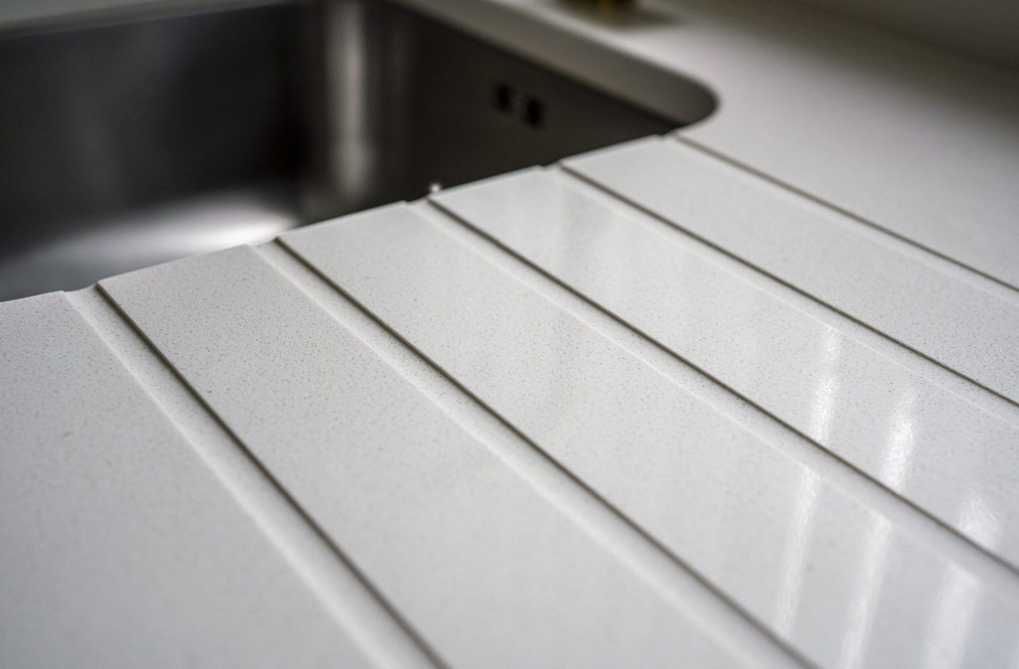 Close-up of Imperial White Quartz drainer grooves beside an inset sink with clean, straight channels