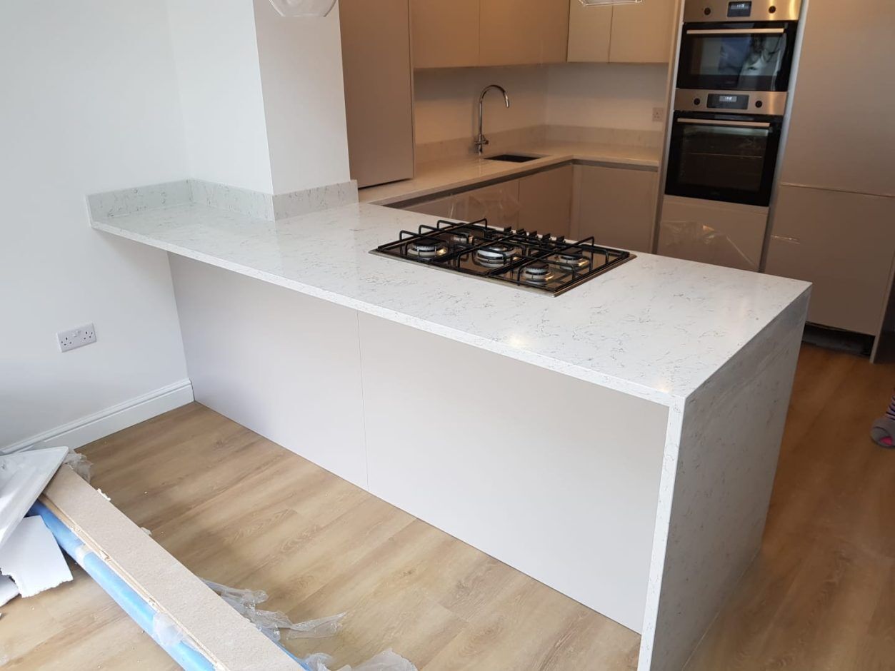 White Arabesque Quartz waterfall island with hob cut-out showing subtle grey marbling on a bright white surface