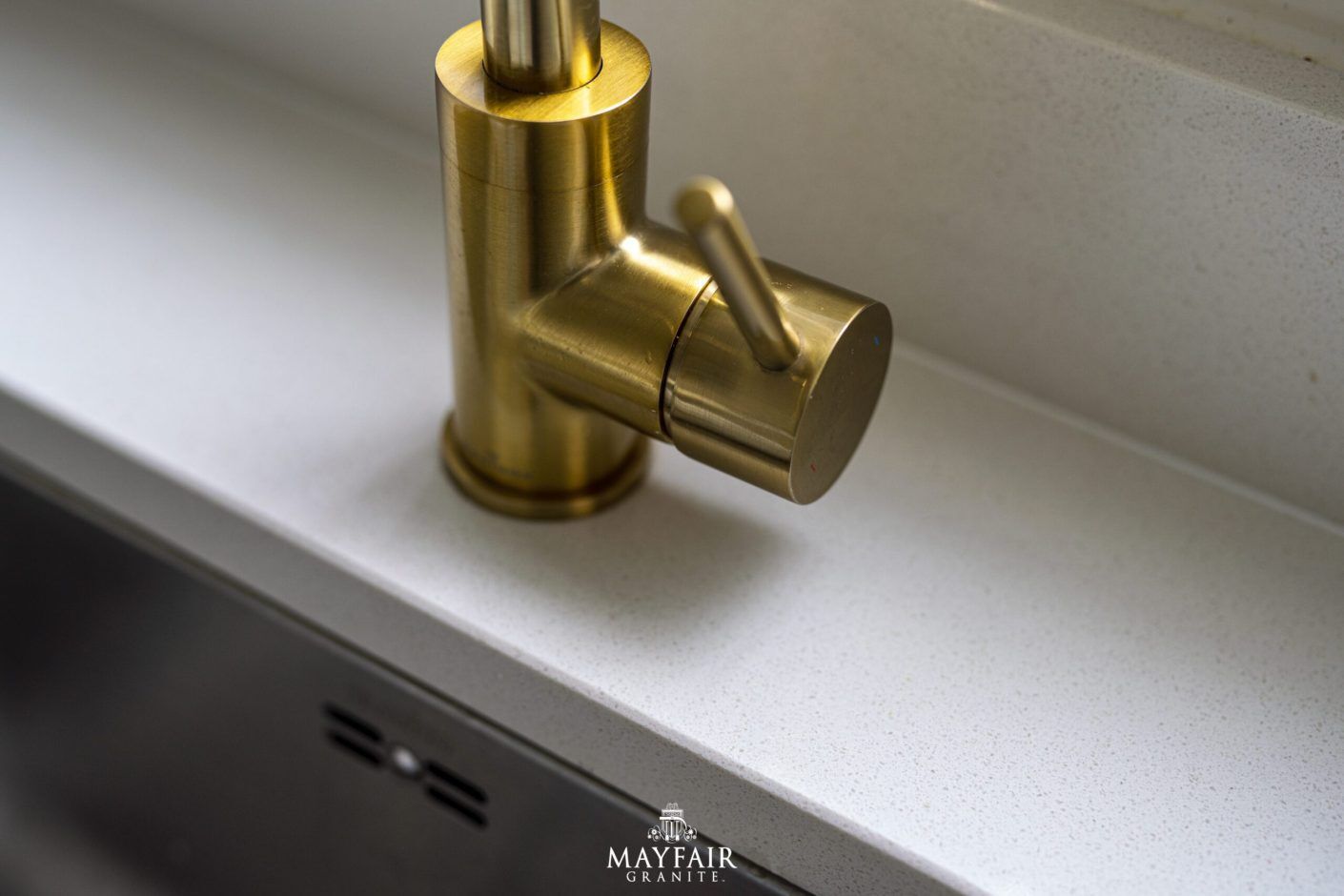 Close-up of a brass tap set into an Imperial White Quartz worktop with a smooth white finish