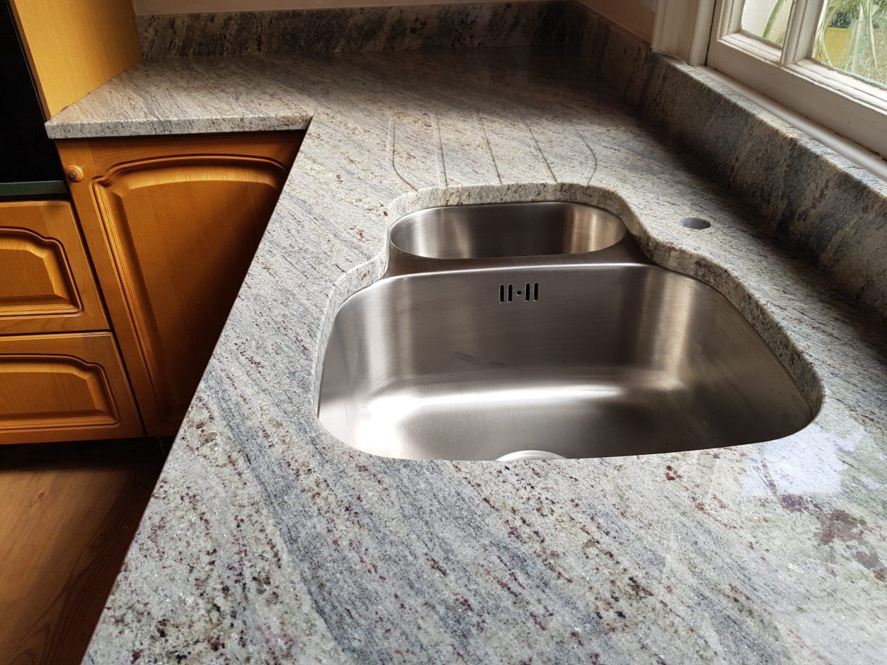 Close up of an undermount sink fitted into Kashmir White Granite worktop, showing the polished Granite surface with soft grey movement around the cut-out.