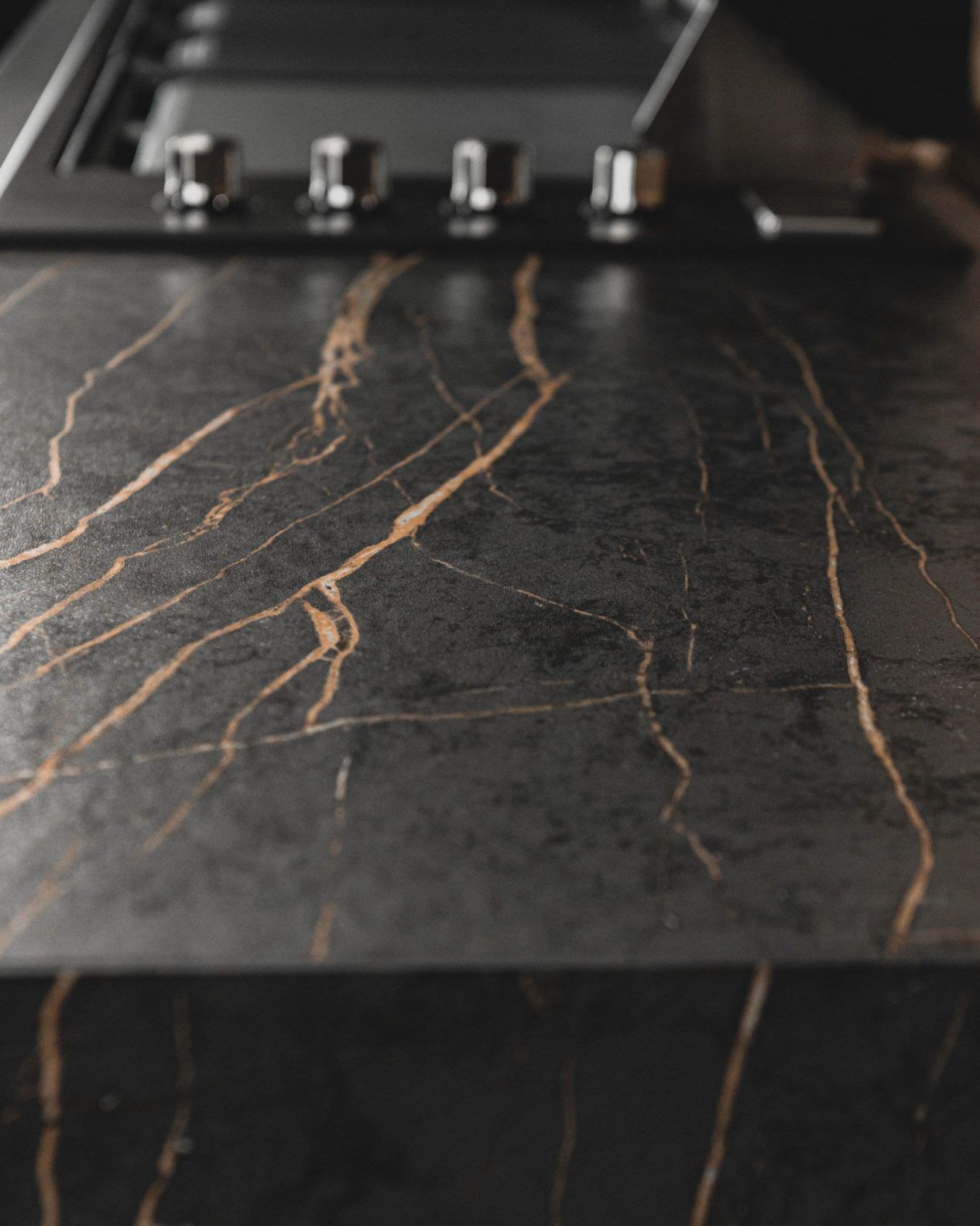 Laurent Porcelain worktop close-up showing dark stone-effect surface with strong gold veining under kitchen lighting.